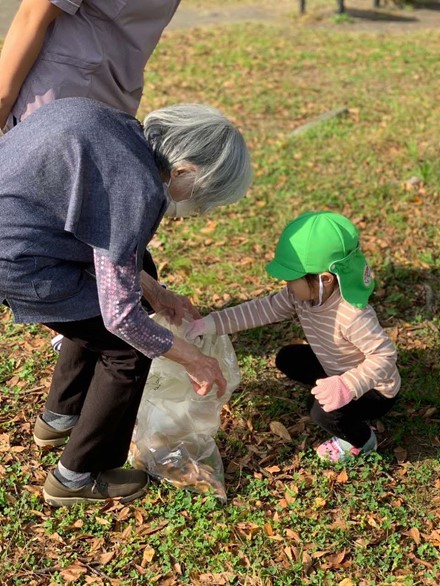 おばあちゃんにごみ袋を持ってもらい、ごみや落ち葉を入れる園児