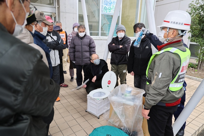 簡易トイレの使い方について説明を聞く参加者